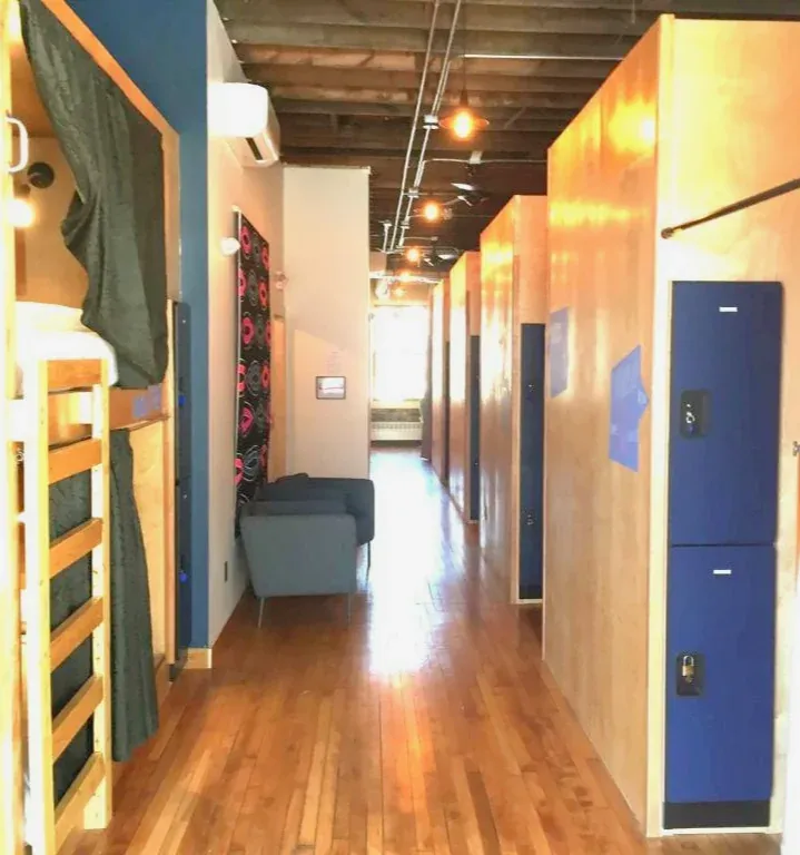 Warm wood dorm corridor lined with sleeping pods and blue lockers