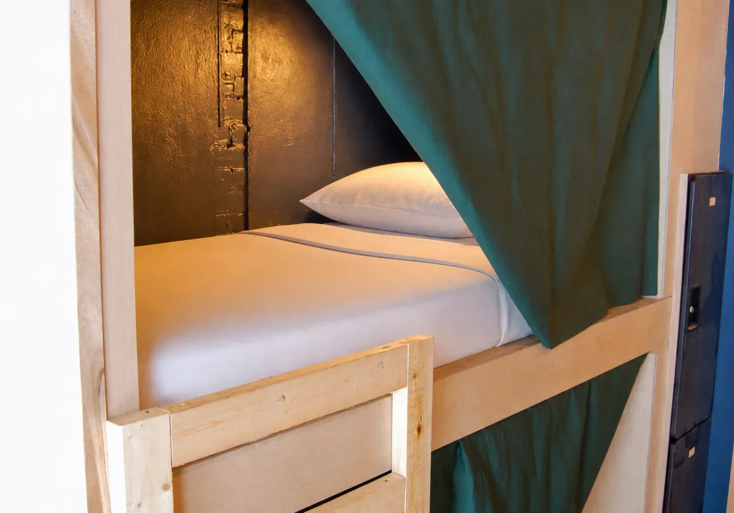 A private sleeping pod at Hostel du Nord with its green privacy curtain pulled open