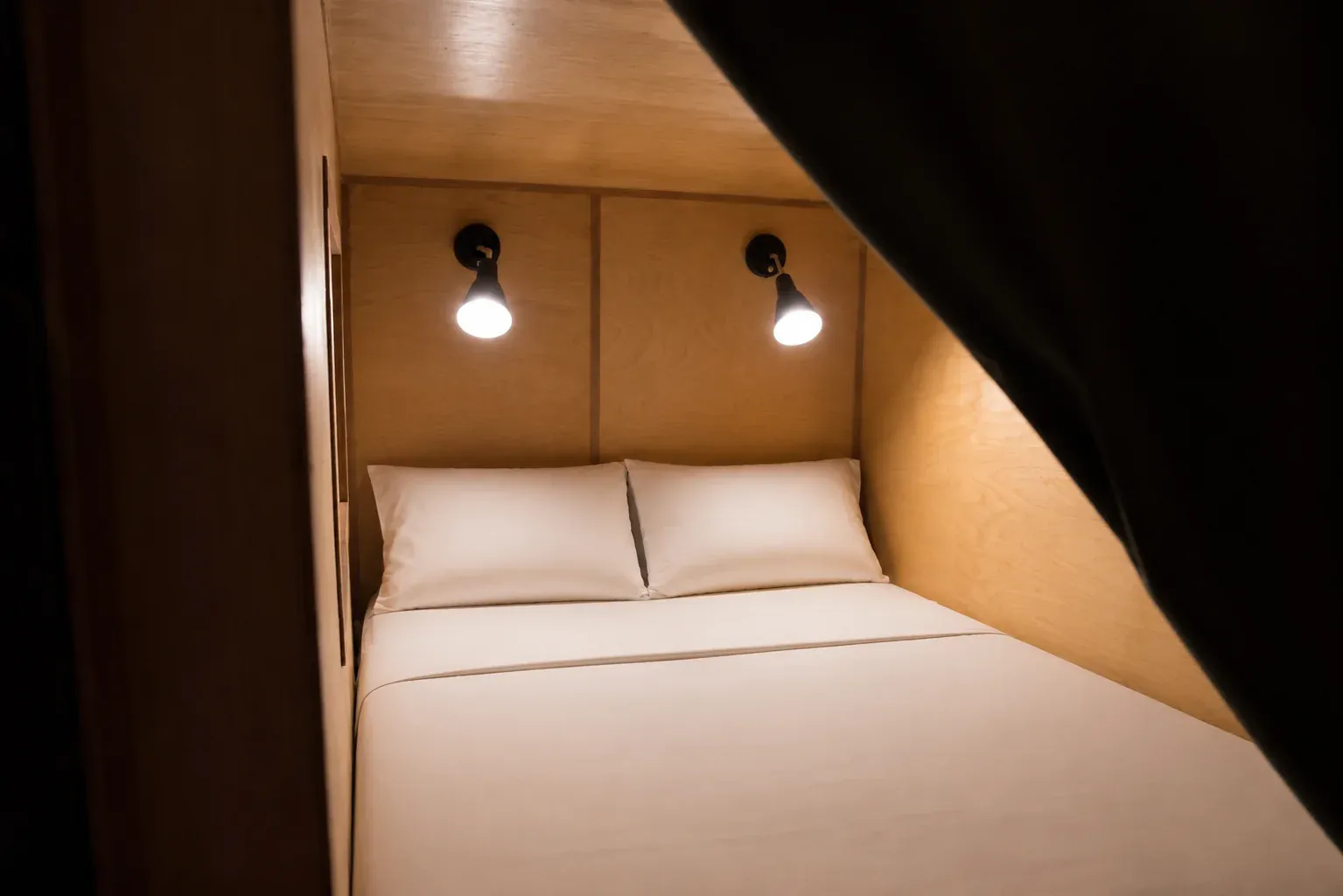 Inside a sleeping pod: made bed, wood panel walls and twin reading lights
